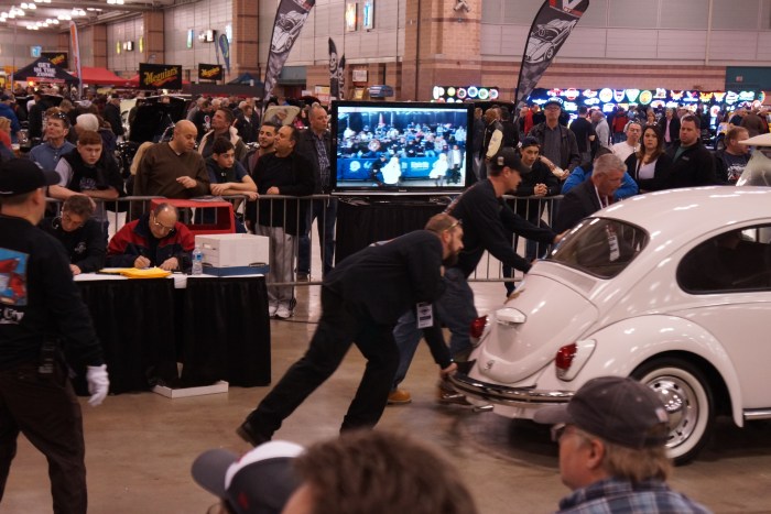 The pushers move a VW Beetle off the block an past the TV screen.